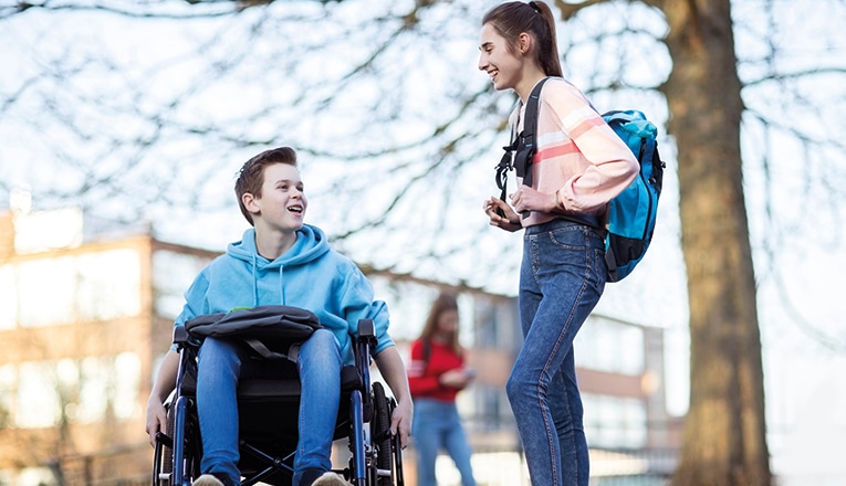 Jongen met duchenne zit in een rolstoel en praat met een klasgenoot