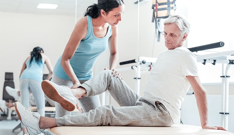 Een fysiotherapeut helpt een man met artrose in zijn knie met zijn oefeningen.